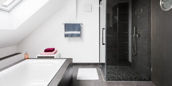 Ein modernes Badezimmer mit einer freistehenden Badewanne und einer eleganten Dusche, die mit dunklen Fliesen gestaltet ist.