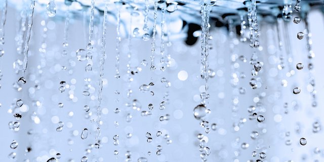 Wassertropfen fallen in einer sanften Bewegung, während sie im Licht funkeln und eine ruhige Atmosphäre schaffen.