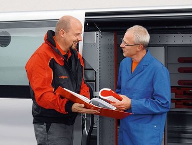 Zwei Männer im Gespräch über Werkzeuge im Lieferwagen Ein Vissmann Mitarbeiter zeigt einem Kunden, einen Ordner vor einem Firmenbulli