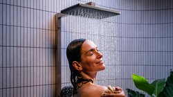 Eine Frau genießt eine erfrischende Dusche, während Wasser sanft über ihr Gesicht fließt und sie entspannt lächelt.