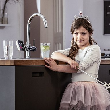 Ein verkleidetes Maedchen steht in der Kueche vor dem Trinkwasserhahn
