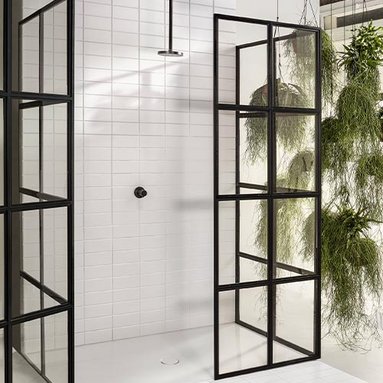 Eine moderne Dusche mit schwarzen Glastüren und weißen Fliesen, umgeben von hängenden Pflanzen für ein frisches Ambiente.