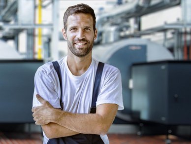 Lächelnder Techniker in einer modernen Industrieumgebung Ein lächelnder Mann in Arbeitskleidung mit verschänkten Armen