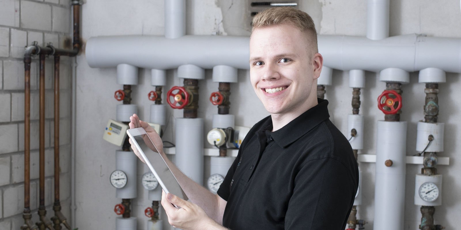 Ein Anlagenmechaniker vor einer Heizungsanlage mit einem Tablet