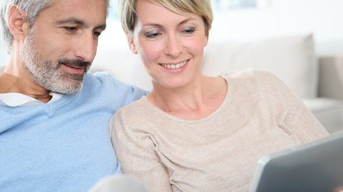 Ein Paaerchen sitzen nebeneinander und schauen auf ein Tablet