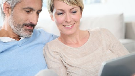 Ein Paaerchen sitzen nebeneinander und schauen auf ein Tablet